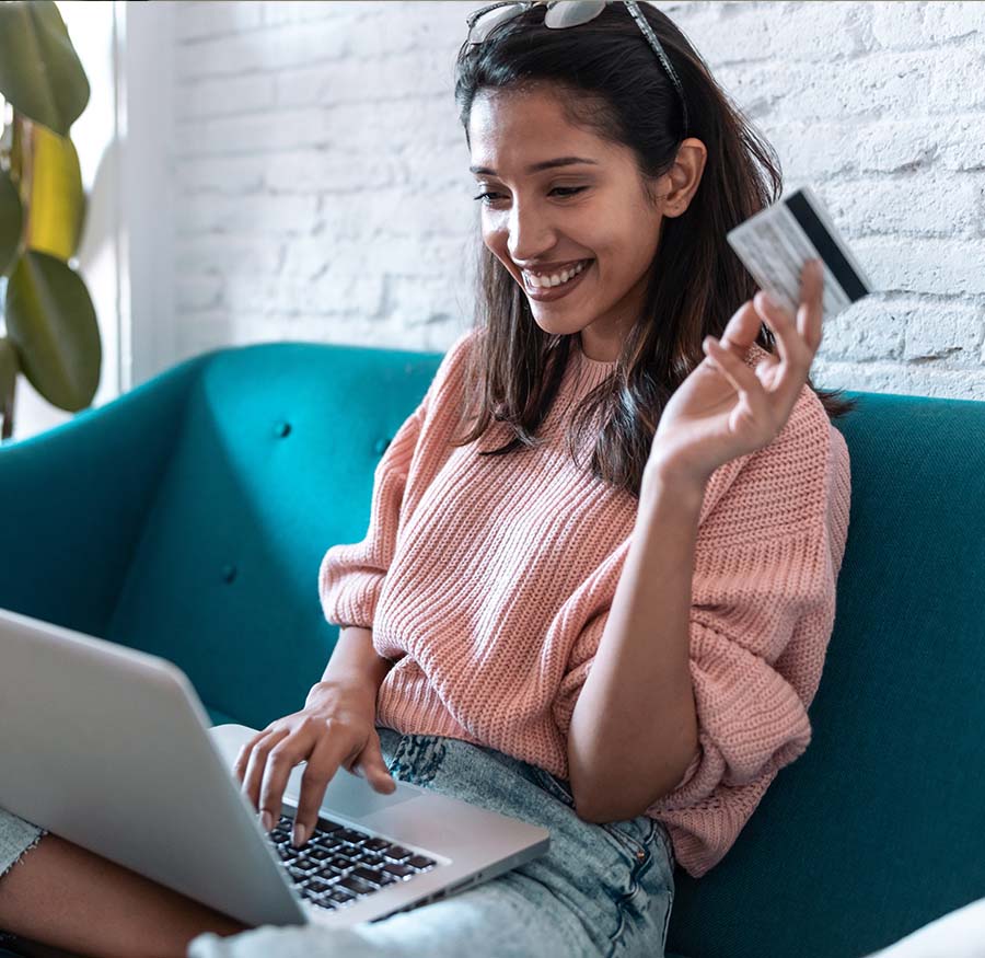 woman on teal couch looking at laptop holding credit card