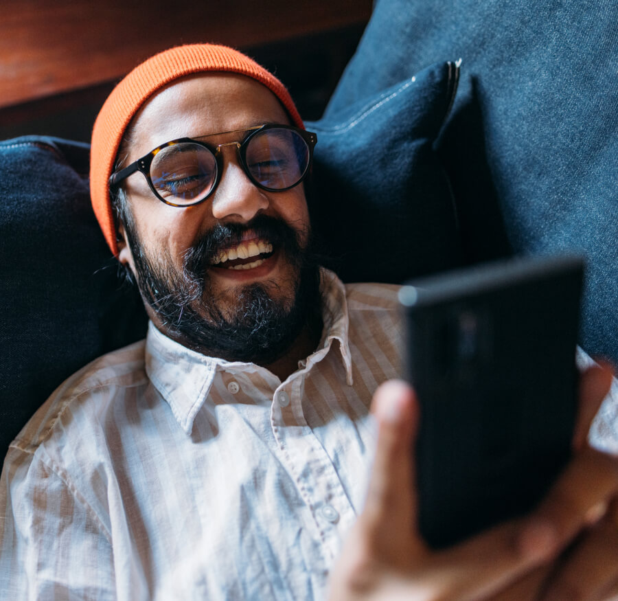 a man wearing glasses laughing while looking at his mobile phone