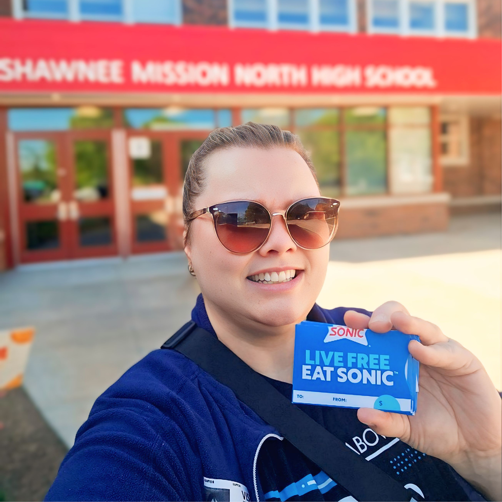 Azura staff posed with Sonic gift card in front of Shawnee Mission North High School