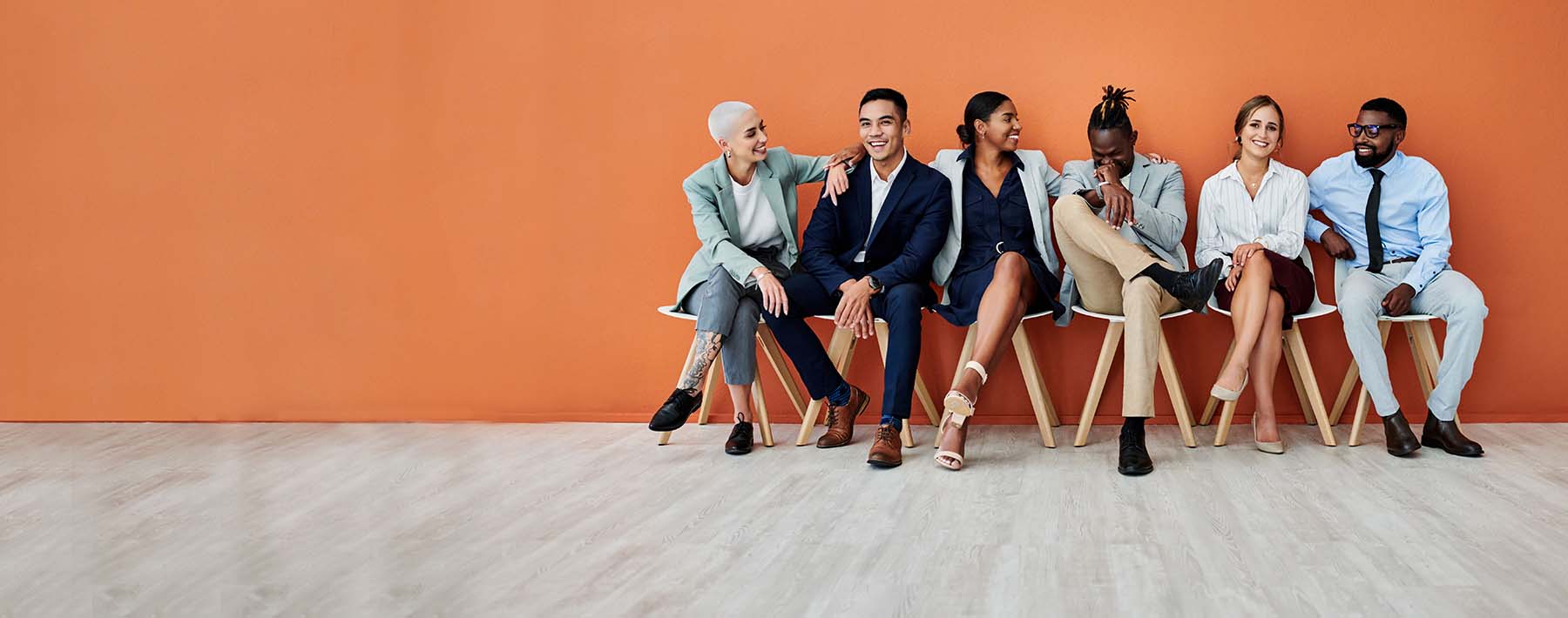 6 professionals sitting in chairs against an orange wall