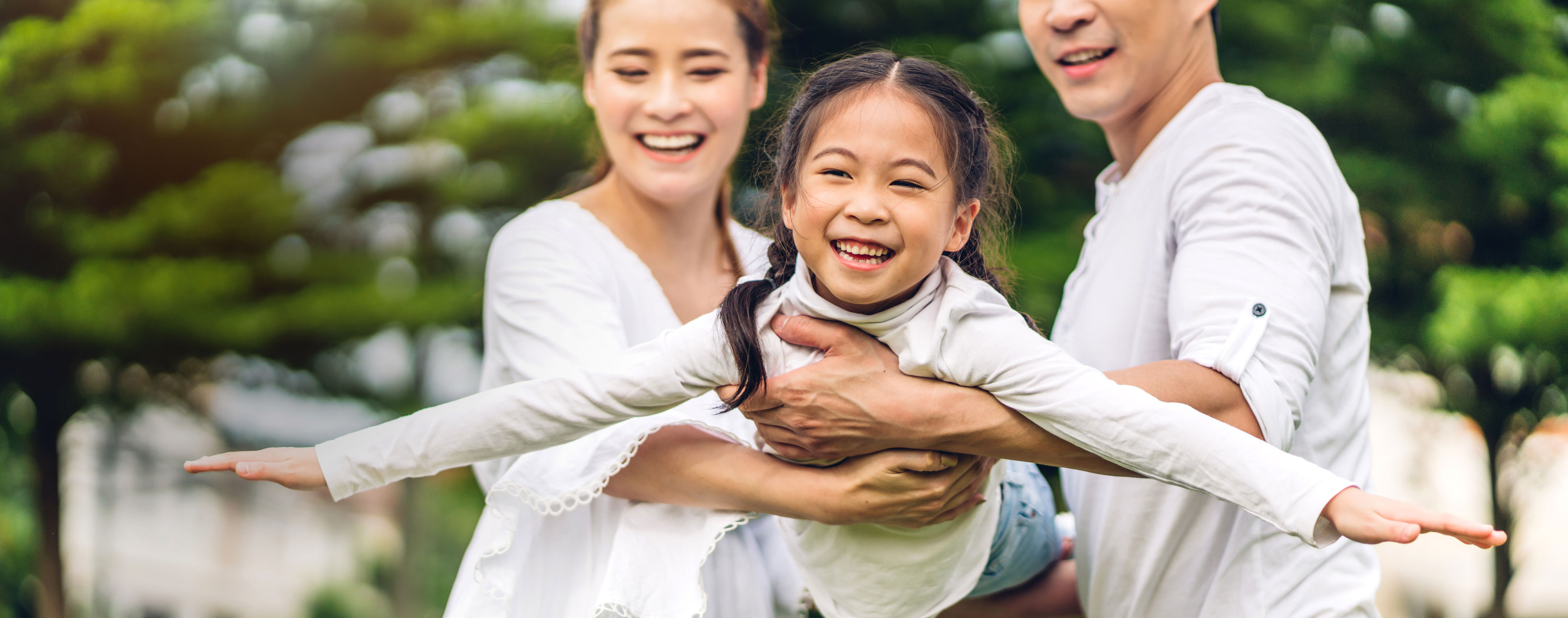 Asian couple holding young daughter her arms out like an airplane