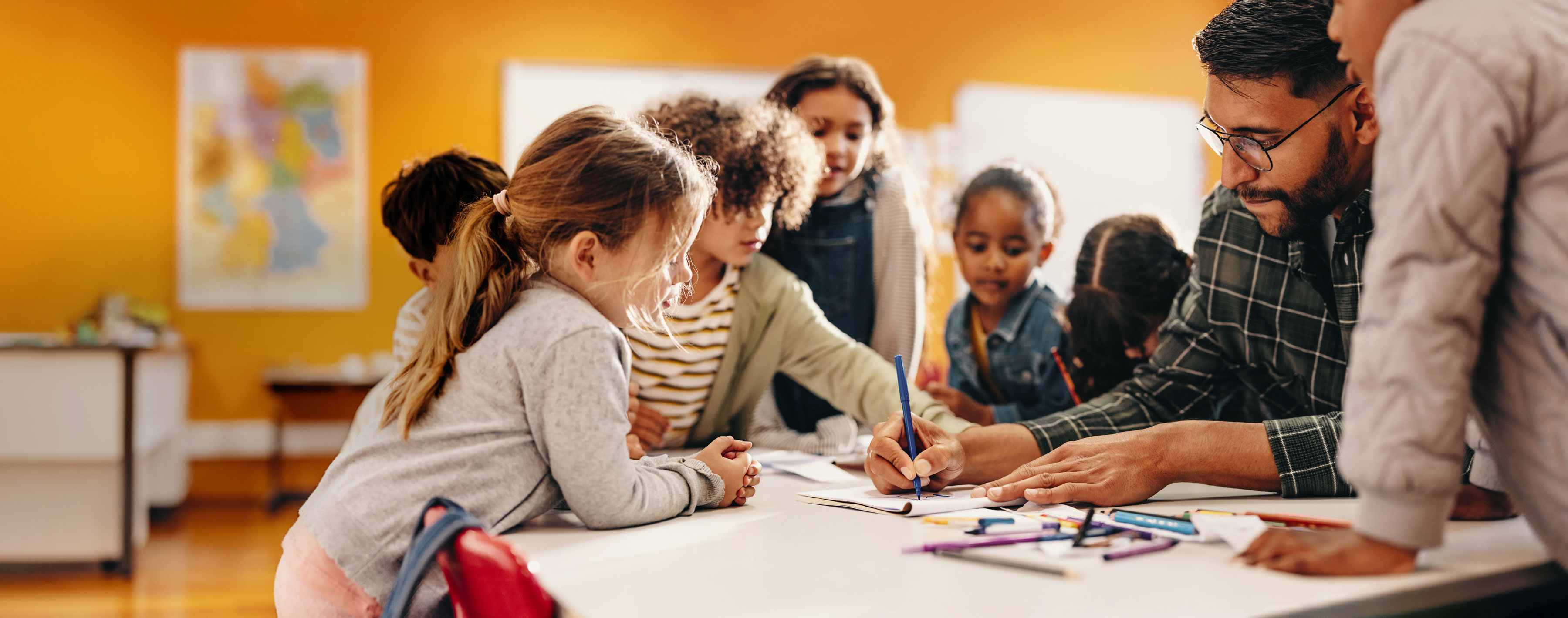 Young students gather around a teacher looking at an assignment together. 