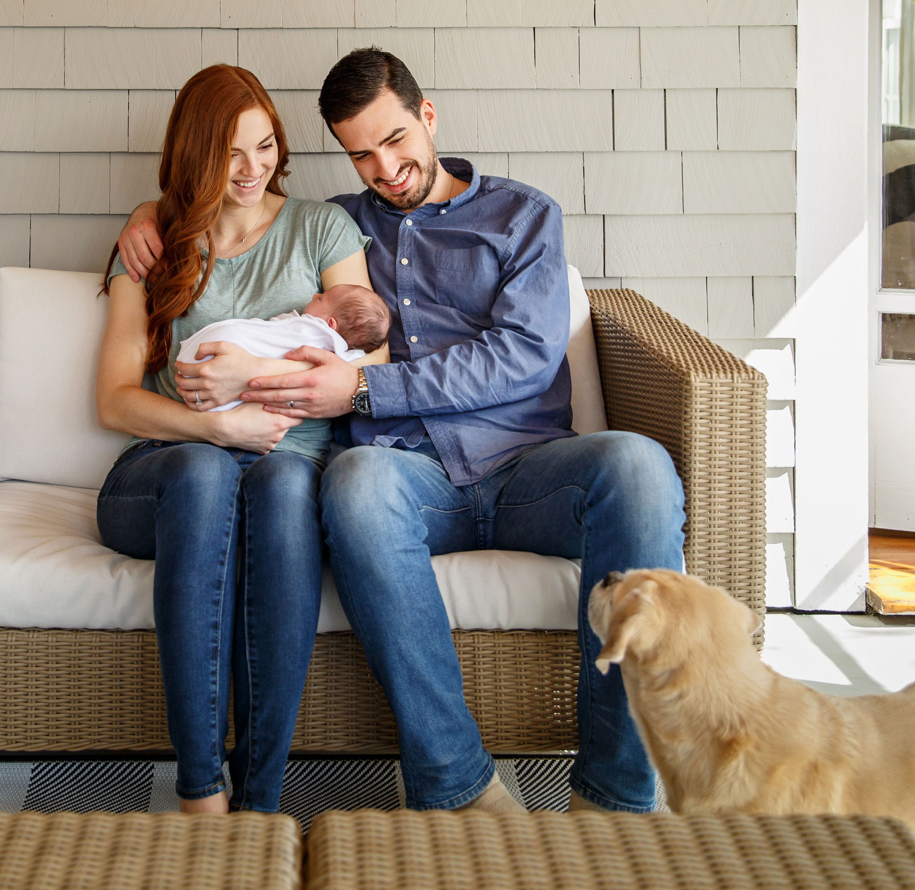 Young couple with an infant and dog sitting on outside on porch