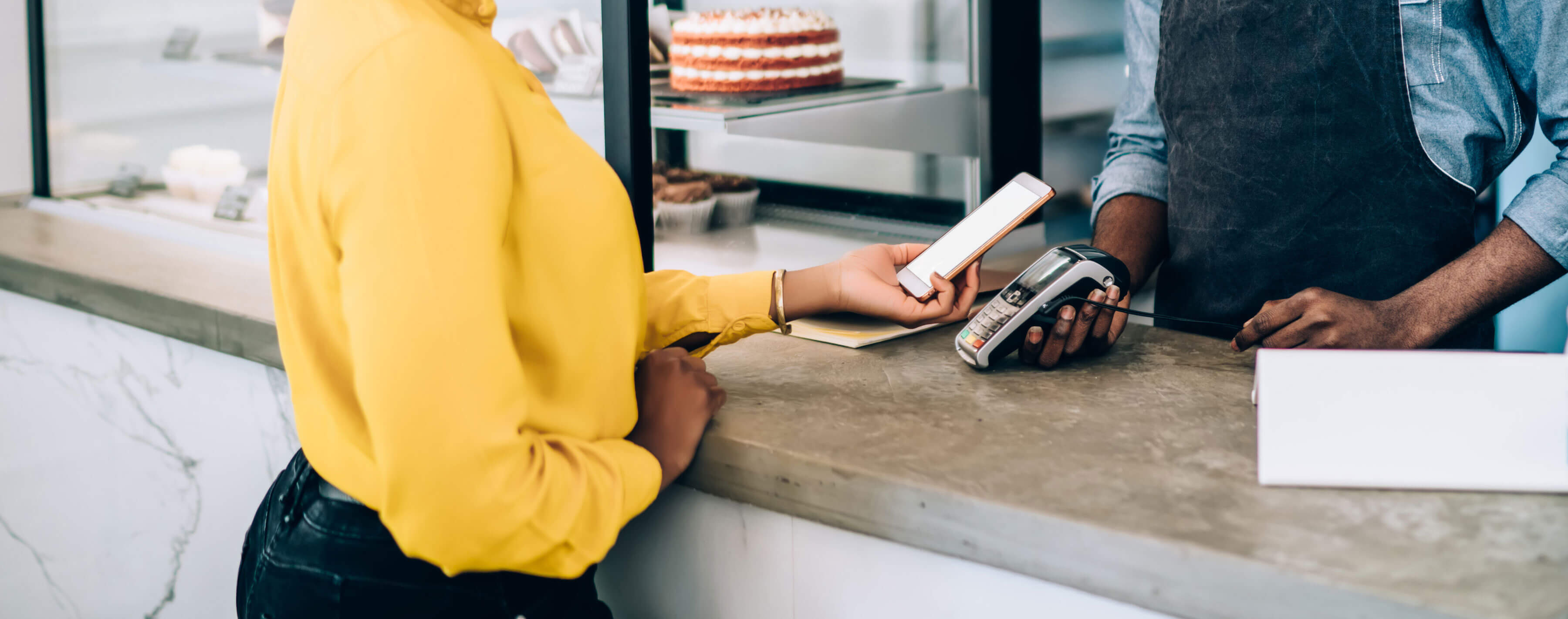 Close up, seller holding terminal and waiting while client making contactless payment with smartphone in modern pastry shop. card reader machine and mobile phone with banking NFC technology