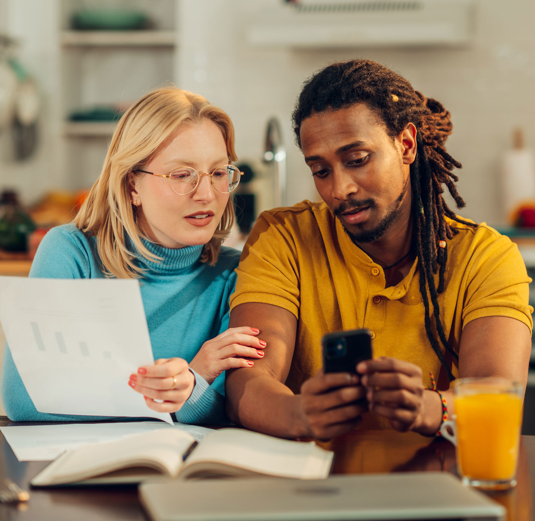 A young multiracial couple at home using a cell phone and reviewing financial papers. 